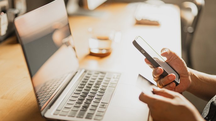 Detailansicht von Smartphone und Karte auf Schreibtisch mit Laptop, symbolisiert unkomplizierte Anpassung der Bankdaten bei ENTEGA.