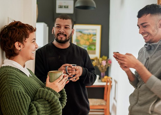 Drei Menschen tauschen sich entspannt in der Küche aus, besprechen Stromverbrauch 3 Personen-Haushalt für mehr Energieeffizienz im Haushalt.