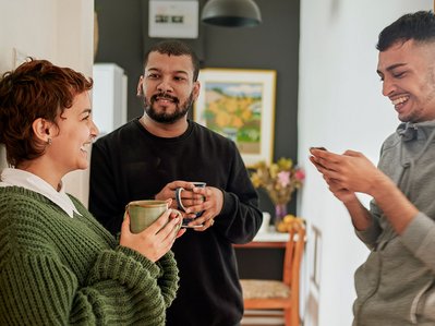 Drei Menschen tauschen sich entspannt in der Küche aus, besprechen Stromverbrauch 3 Personen-Haushalt für mehr Energieeffizienz im Haushalt.