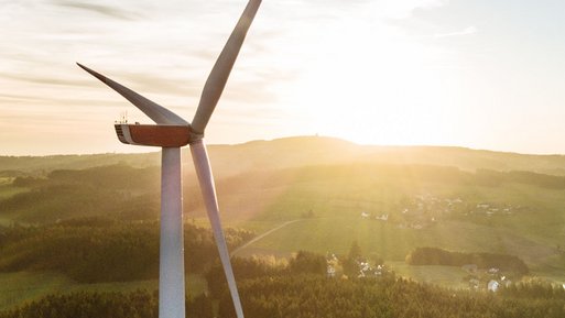 Windkraftanlage unter der aufgehenden Sonne, umgeben von Wäldern und Feldern.