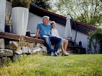 Familie entspannt im Garten vor dem Eigenheim, steht für Tipps und Kosten zum ENTEGA Glasfaseranschluss.