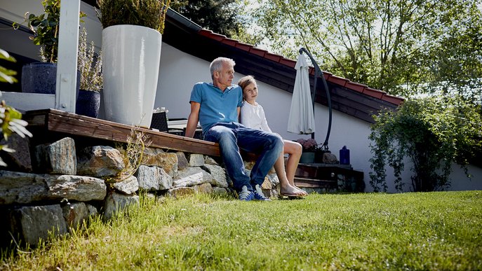 Familie entspannt im Garten vor dem Eigenheim, steht für Tipps und Kosten zum ENTEGA Glasfaseranschluss.
