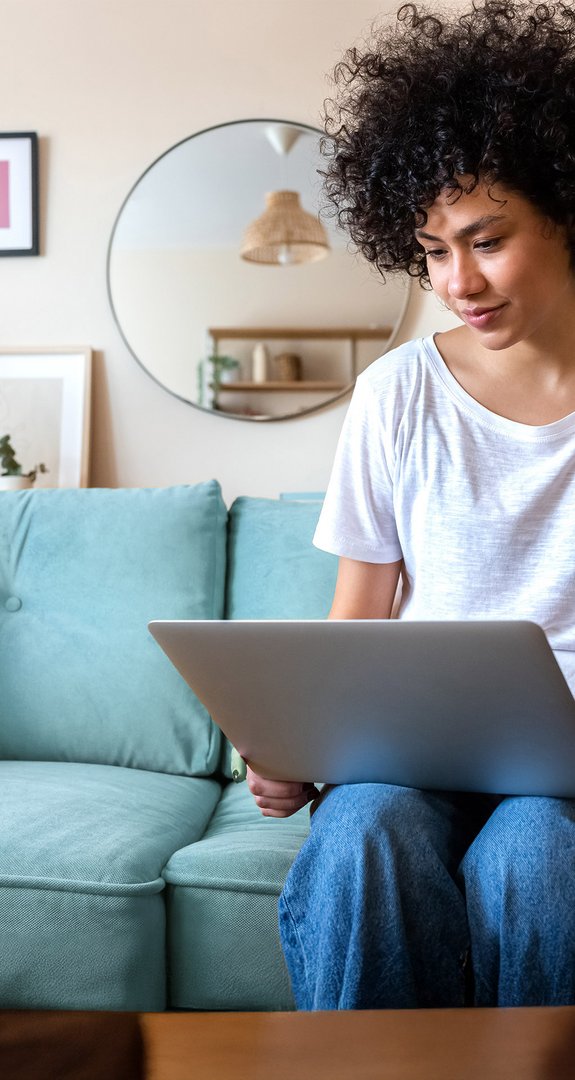 Person sitzt auf Sofa mit Laptop und informiert sich über ENTEGA-Kündigung per E-Mail, Wohnumgebung mit moderner Dekoration.