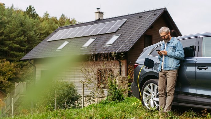 Bild zeigt einen Mann, der sein Elektroauto lädt und sich während der Ladezeit mit seinem Handy beschäftigt.