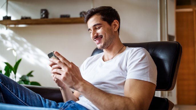 Lächelnder Mann sitzt entspannt im Sessel und schaut auf sein Smartphone. Symbolisiert Informationen zu ENTEGA Tarifen und weitern Themen in der FAQ-Übersicht.