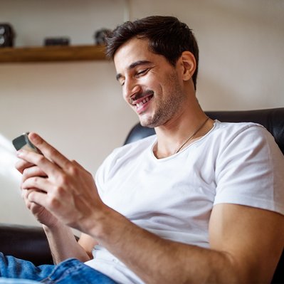 Lächelnder Mann sitzt entspannt im Sessel und schaut auf sein Smartphone. Symbolisiert Informationen zu ENTEGA Tarifen und weitern Themen in der FAQ-Übersicht.
