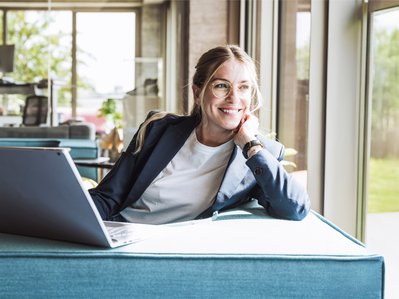 Frau am Laptop in modernem Büro, lächelnd und zufrieden. Symbolisiert sichere, leistungsstarke Cloud-Anbindung mit ENTEGA Cloud Connect.