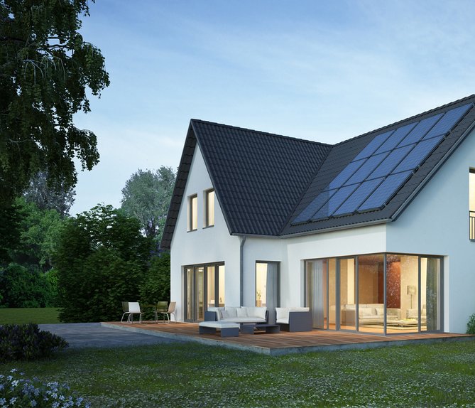 Modernes Einfamilienhaus mit Solarmodulen auf dem Dach und Terrasse, umgeben von üppigem Grün.