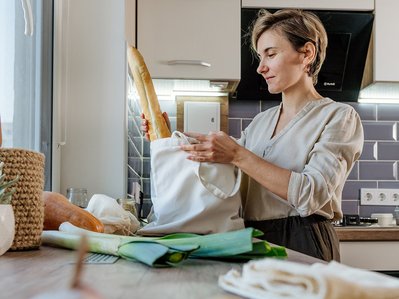 Müllvermeidung Tipps: Eine Frau nutzt wiederverwendbare Beutel für Lebensmittel, um Plastikmüll beim Einkaufen in der Küche zu reduzieren.