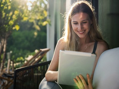 Frau sitzt draußen vor einem Tablet. Sonnenlicht im Hintergrund. Kontext: Nutzung dynamischer Stromtarife per App.