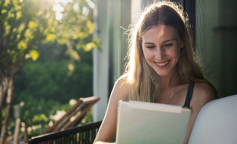 Frau sitzt draußen vor einem Tablet. Sonnenlicht im Hintergrund. Kontext: Nutzung dynamischer Stromtarife per App.
