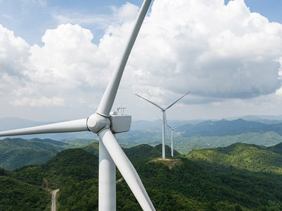 Windräder als Alternative Energiequellen auf grünen Hügeln, drei Anlagen in Reihe, tagsüber, bewölkter Himmel, nachhaltige Stromerzeugung.