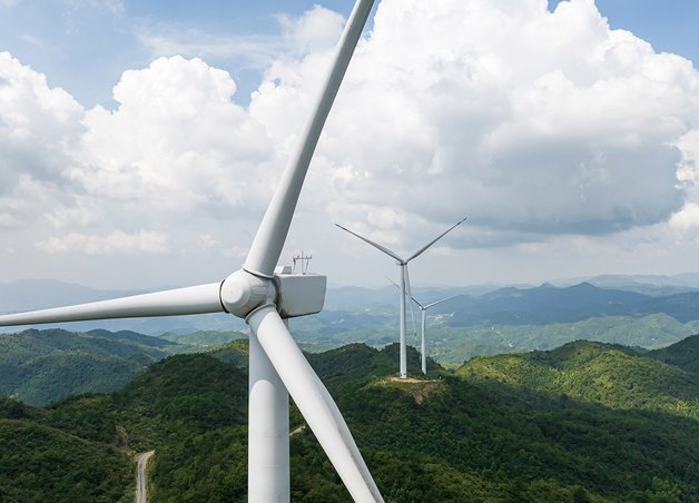Windräder als Alternative Energiequellen auf grünen Hügeln, drei Anlagen in Reihe, tagsüber, bewölkter Himmel, nachhaltige Stromerzeugung.