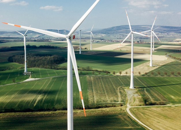 Mehrere Windkraftanlagen mit langen Rotoren auf Feldern, Windkraftanlage Leistung im Fokus, ländliche Umgebung, Energiegewinnung.