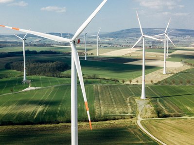 Mehrere Windkraftanlagen mit langen Rotoren auf Feldern, Windkraftanlage Leistung im Fokus, ländliche Umgebung, Energiegewinnung.