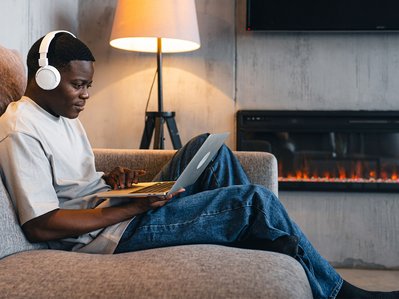 Person entspannt mit Laptop und Kopfhörern auf Couch, Geräte im Hintergrund im Standby; Thema Standby Stromverbrauch im Alltag.