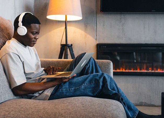 Person entspannt mit Laptop und Kopfhörern auf Couch, Geräte im Hintergrund im Standby; Thema Standby Stromverbrauch im Alltag.