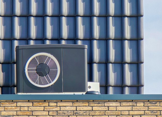 Graue Luftwärmepumpe mit großem Ventilator vor Klinkermauer, Thema: Luftwärmepumpe Kosten, Gebäudetechnik.