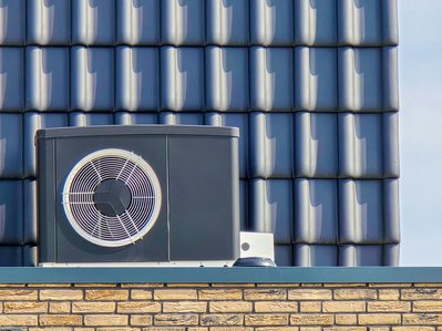 Graue Luftwärmepumpe mit großem Ventilator vor Klinkermauer, Thema: Luftwärmepumpe Kosten, Gebäudetechnik.