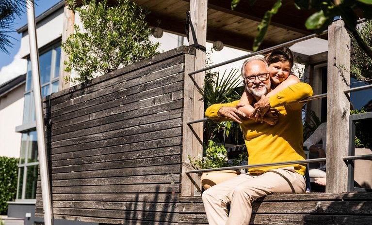 Mann und Kind lachen auf Terrasse, umgeben von Pflanzen. Symbolisiert sorgenfreie Zeit durch zuverlässige Heizungswartung.