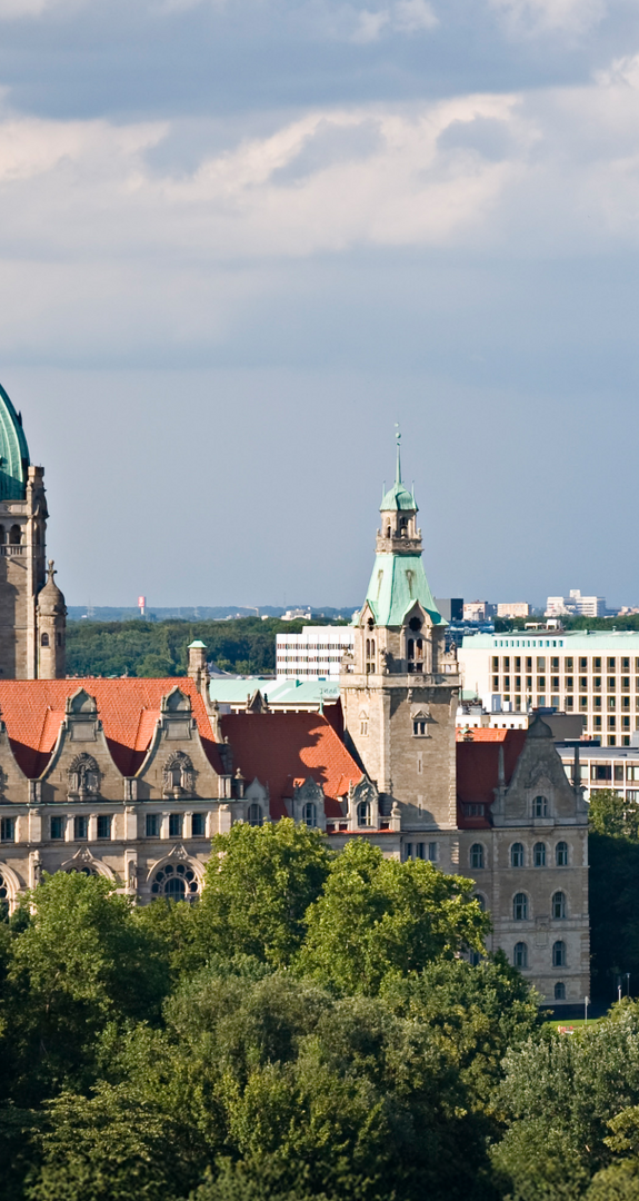 Historisches Rathaus Hannover vor moderner Skyline, viel Grün im Vordergrund; betont die Bedeutung von Ökostrom Hannover für die Stadt.