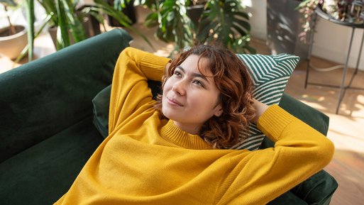 Lächelnde Person liegt auf einem grünen Sofa, umgeben von Pflanzen, Ausdruck von Zufriedenheit mit Wechselprämien und Preisgarantien.