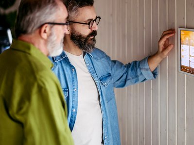 Zwei Personen steuern Nachtstrom vs Tagstrom am Smart-Home-Panel mit Zahlen, Licht- und Klima-Symbolen im modernen Raum.