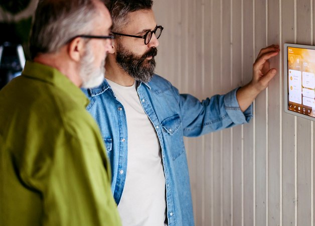 Zwei Personen steuern Nachtstrom vs Tagstrom am Smart-Home-Panel mit Zahlen, Licht- und Klima-Symbolen im modernen Raum.