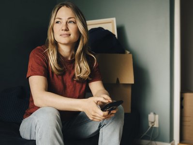 Eine Frau mit Smartphone sitzt zwischen Kartons in der Wohnung. Sie wartet beim Umzug auf die Strom Endabrechnung und finalen Zählerstand.